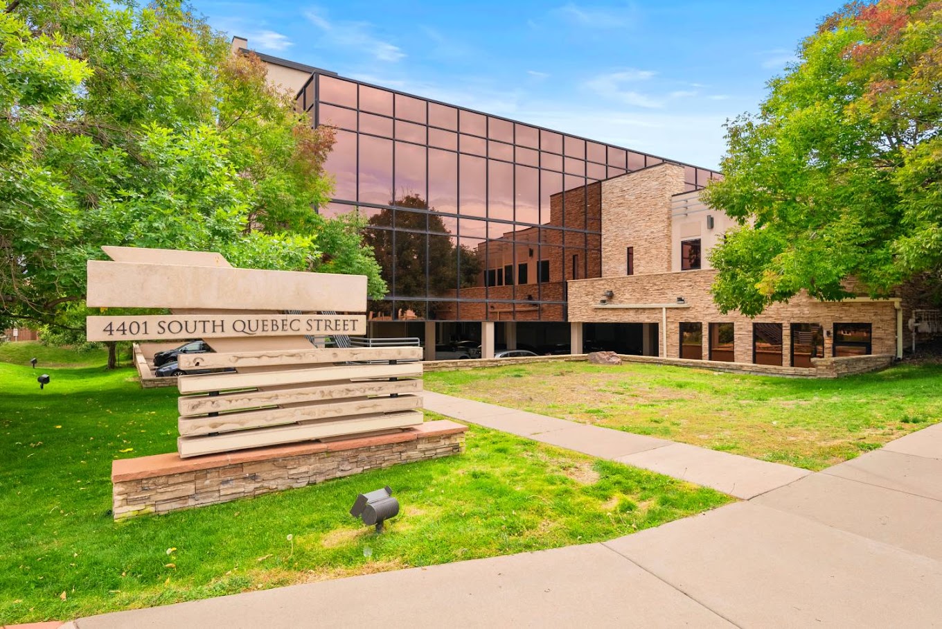 Modern glass-front office building with a large sign on a green lawn.