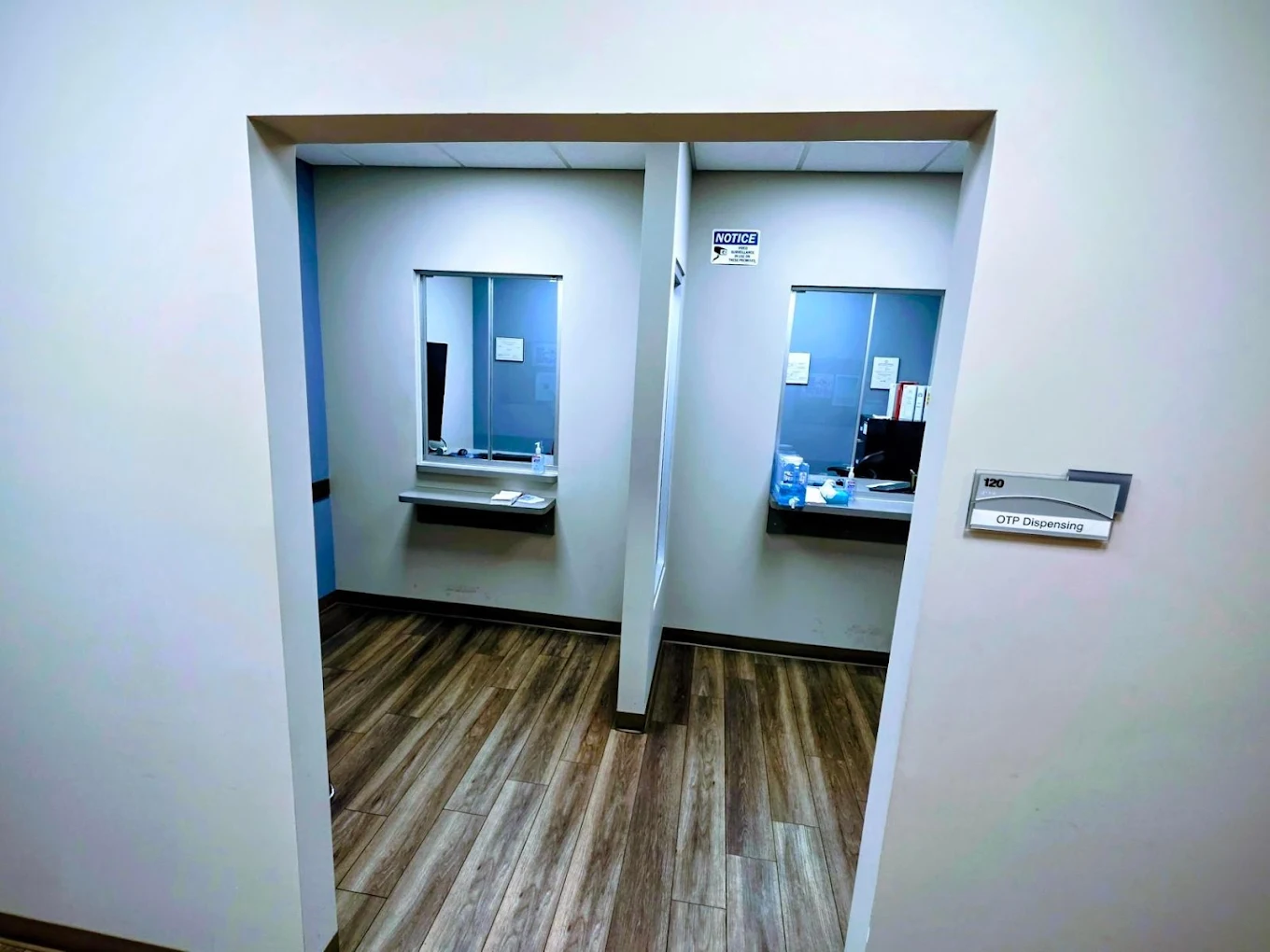 BrightView Health clinical consultation room with computer workstation, office chair, two patient chairs, side table, framed artwork, and blue accent wall