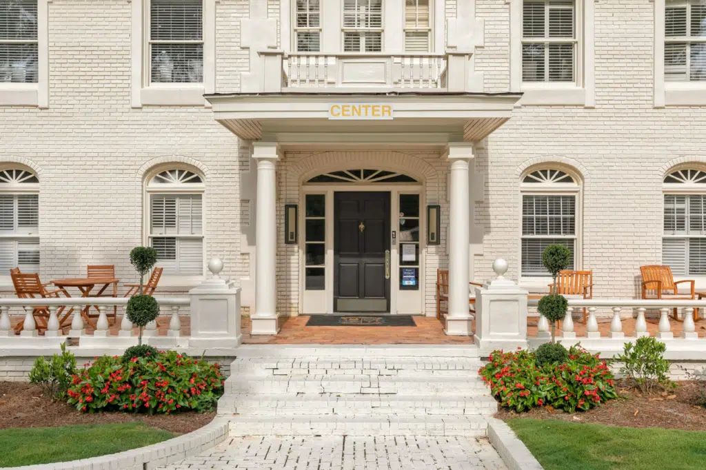 Front entrance of rehab center with white brick exterior and garden seating.