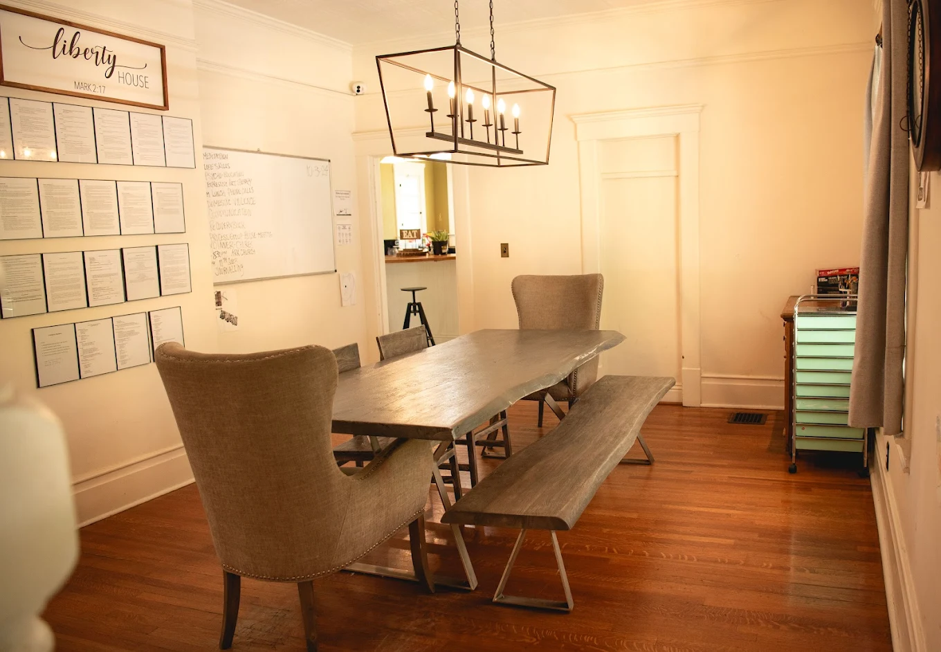 Rustic dining room with long wooden table, benches, and wall of framed documents