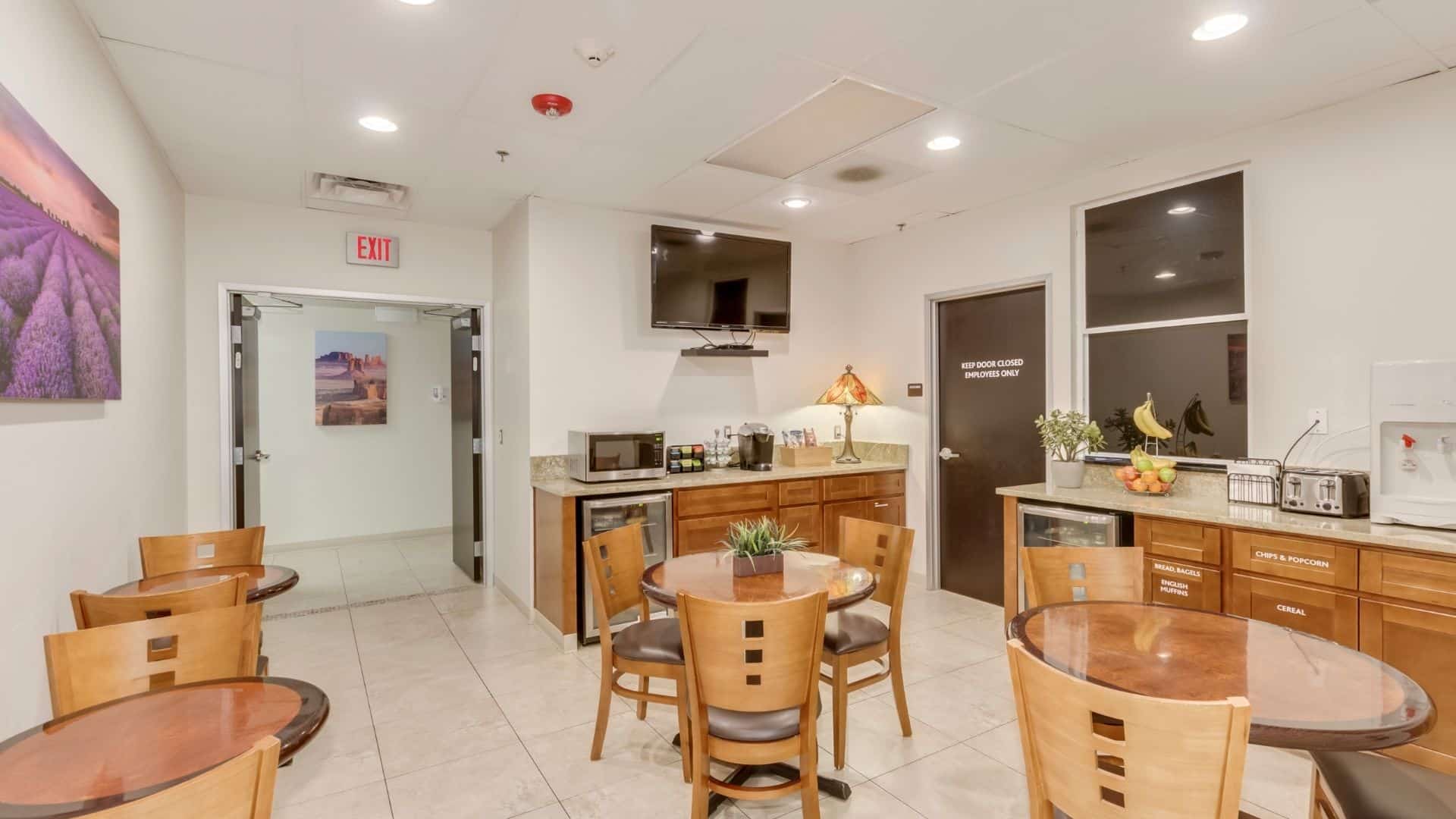Dining area with tables and chairs arraged next to kitchen with a TV.