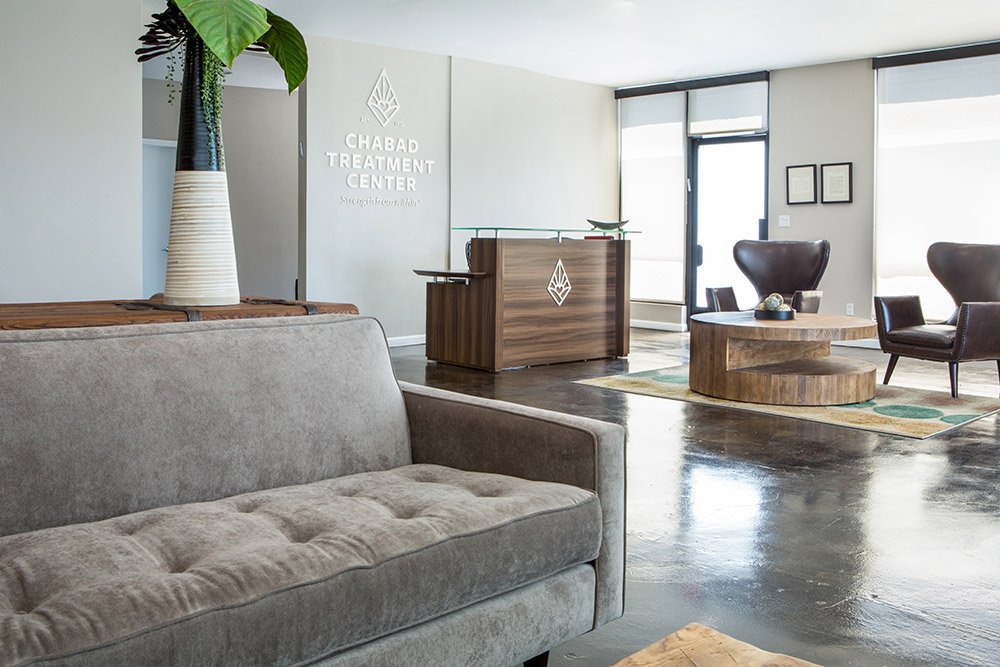 Reception area with couch, chairs, and wooden desk at Chabad Treatment Center