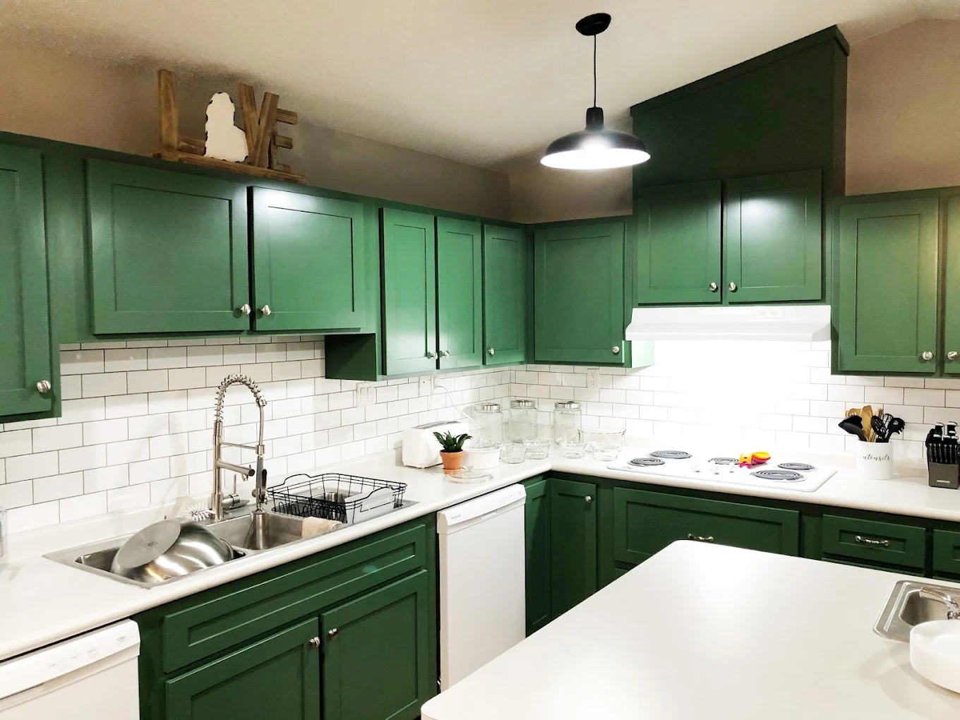 Community kitchen with green cabinets and white tile backsplash