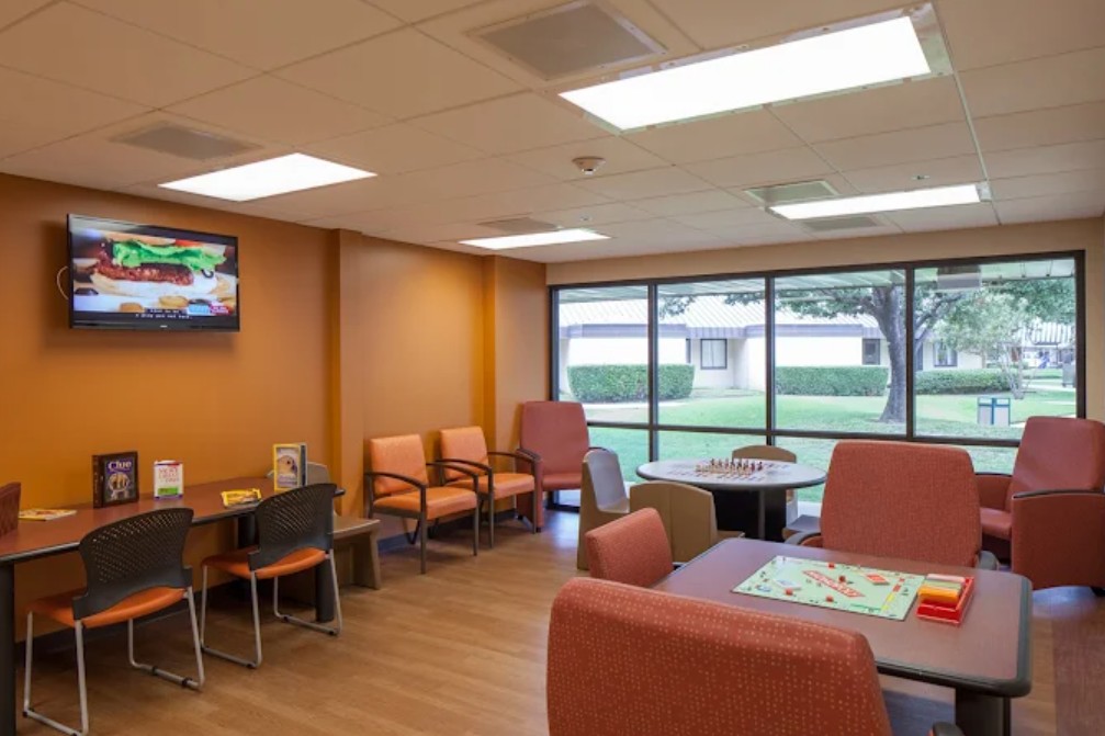 Comfortable patient lounge with seating, board games, television, and large windows overlooking landscaped grounds