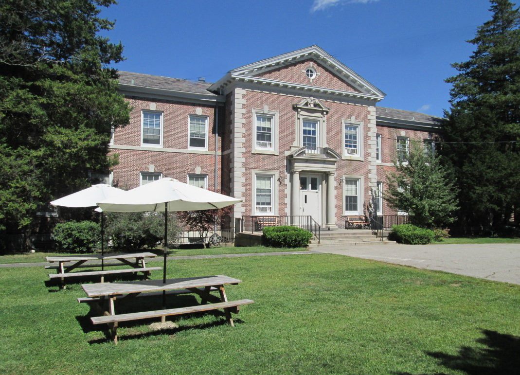 Two-story brick building with picnic tables and umbrellas on lawn
