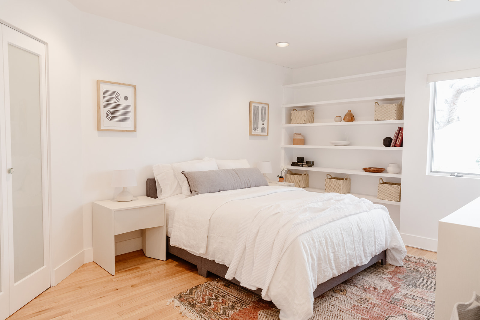 Minimalist bedroom with white decor, built-in shelving, and natural light.