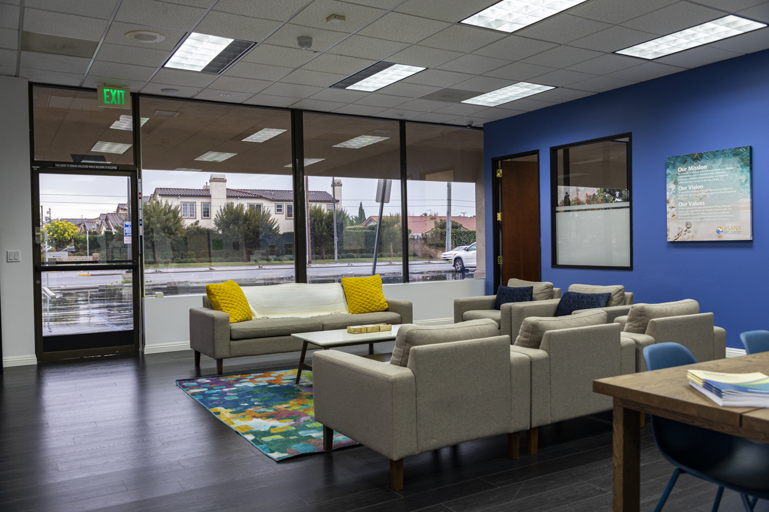 Rehab center lounge with large windows, neutral seating, and a blue wall.