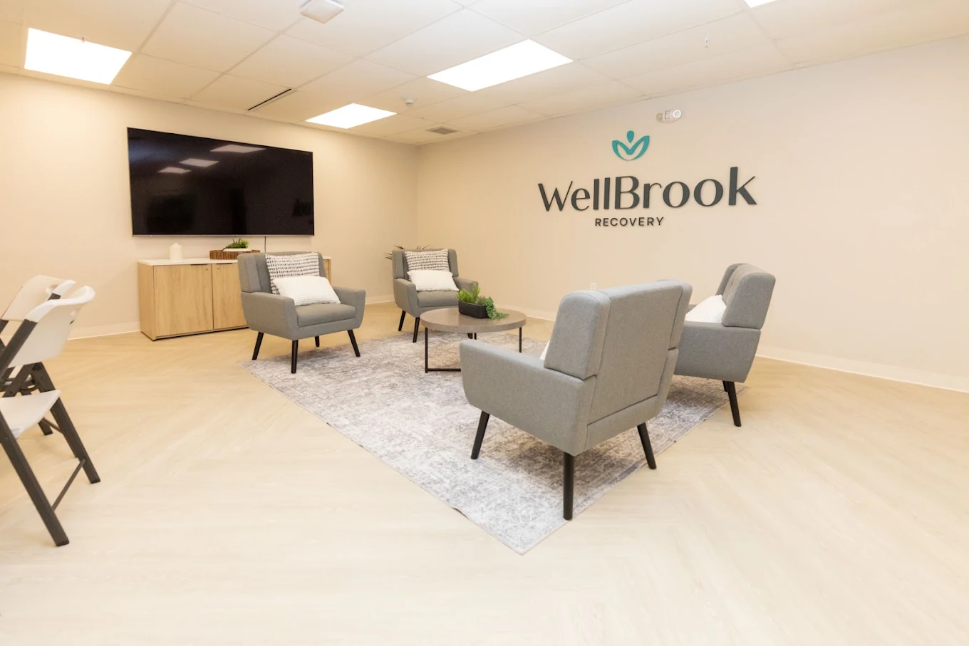 Meeting room with armchairs, television, and facility logo