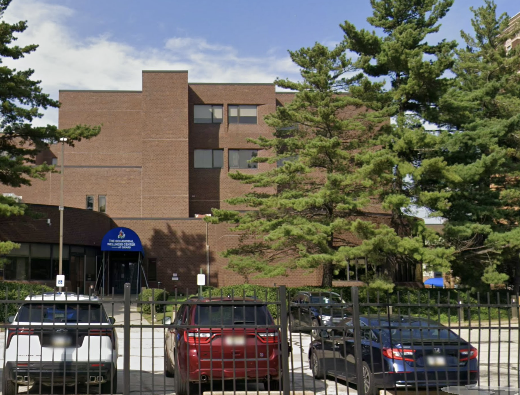 Multi-story brick building with blue entrance awning and parking lot