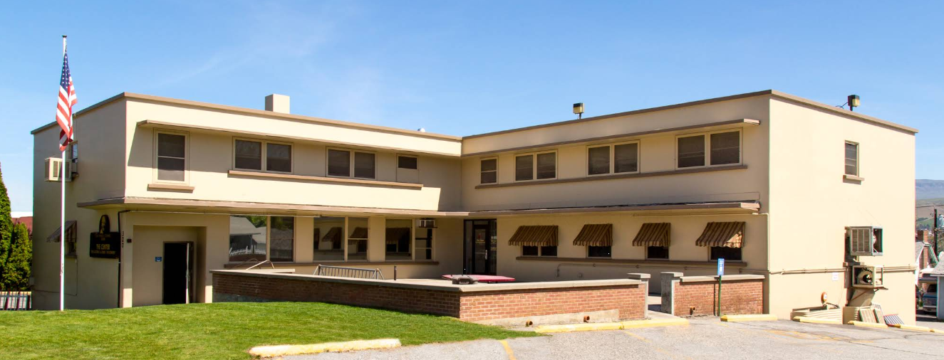 Two-story beige rehab facility with lawn and flagpole