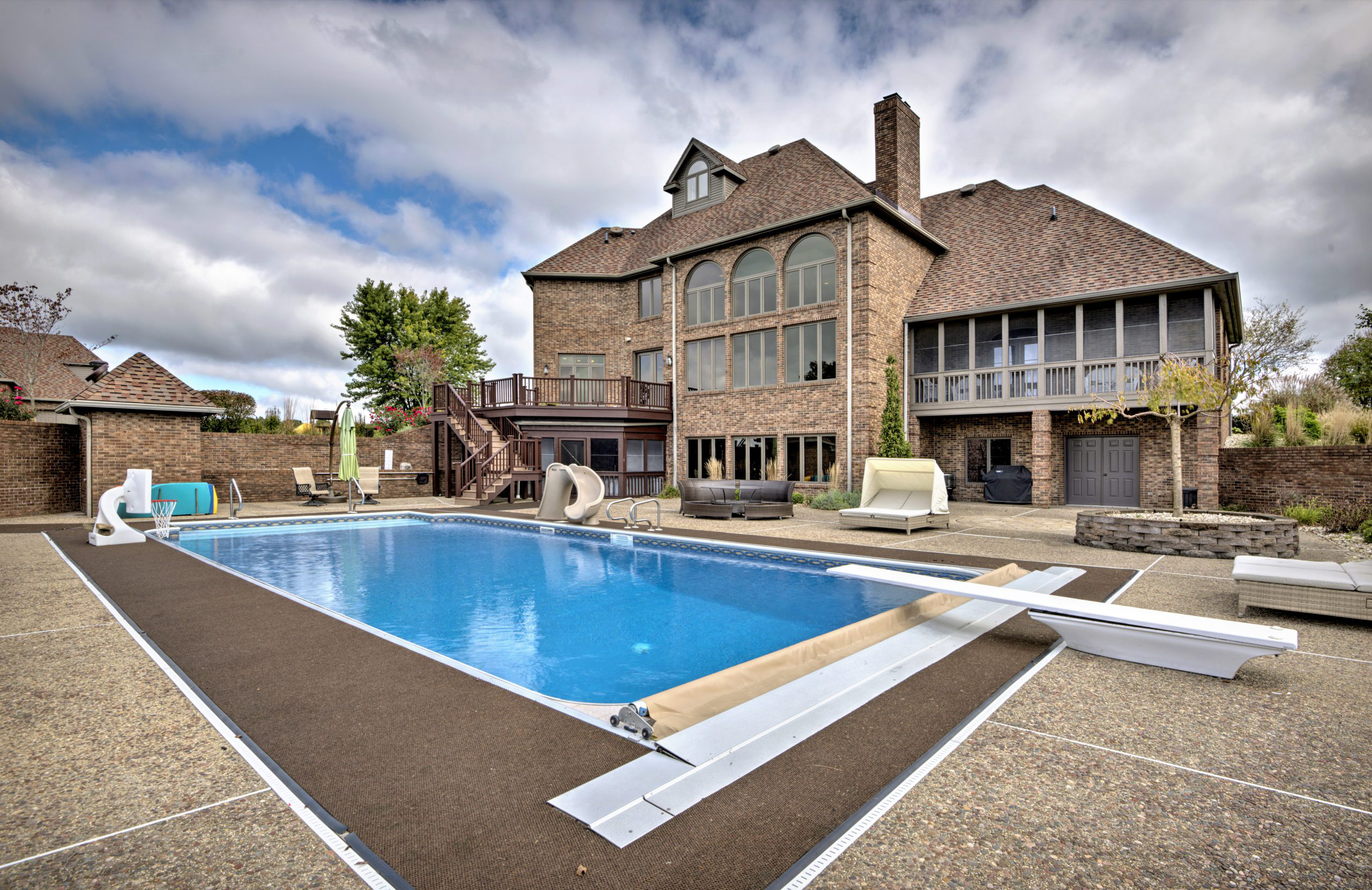 Outdoor pool with lounge chairs and large brick residence