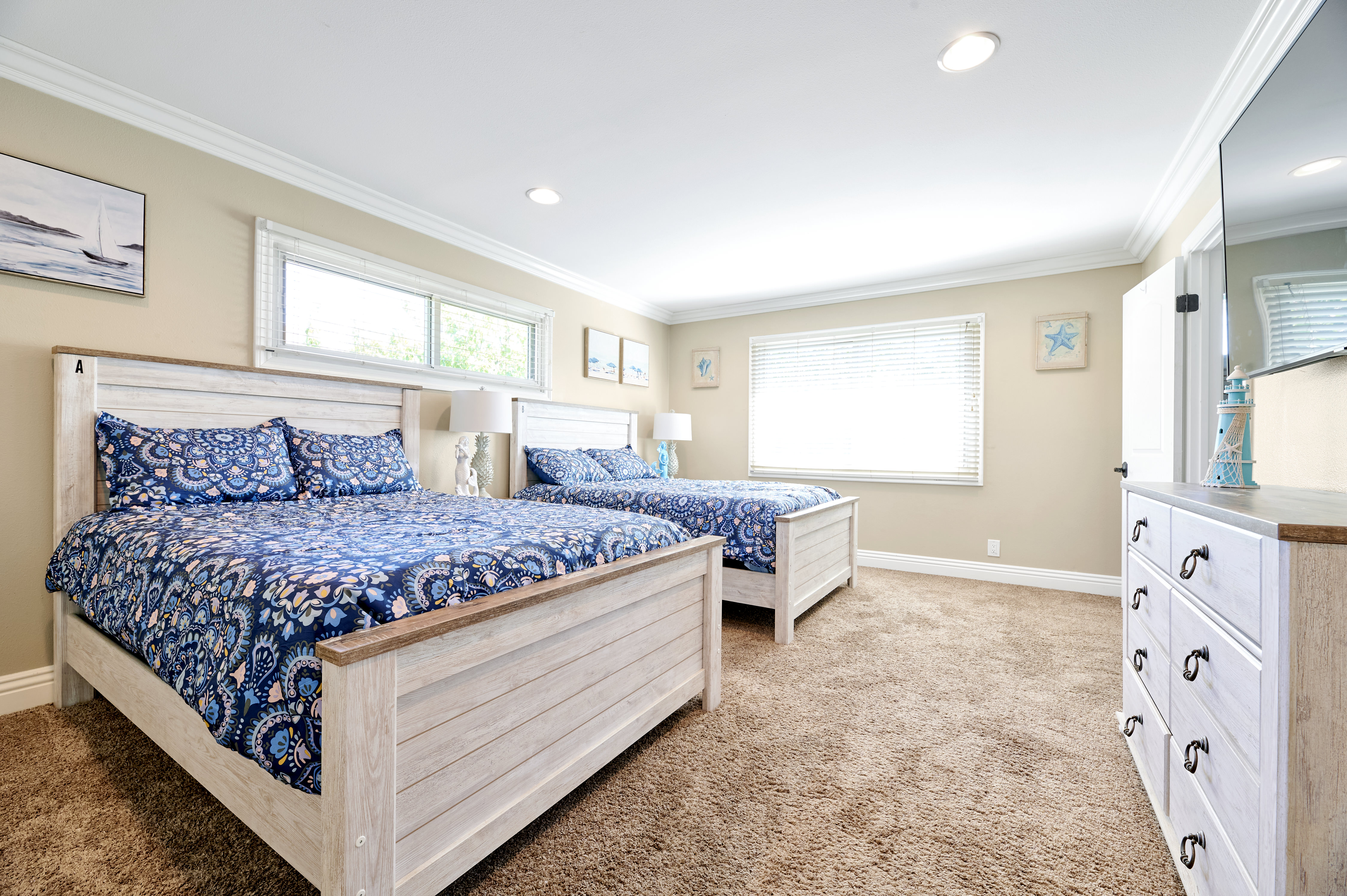 A bright and spacious bedroom featuring two cozy beds with blue patterned bedding, large windows, and soft carpet flooring, creating a relaxing ambiance.