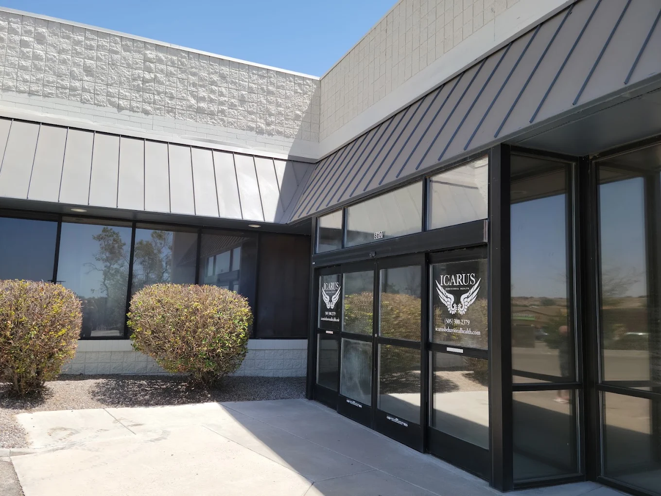 Main entrance to Icarus Behavioral Health with glass doors, exterior windows, and landscaped shrubs