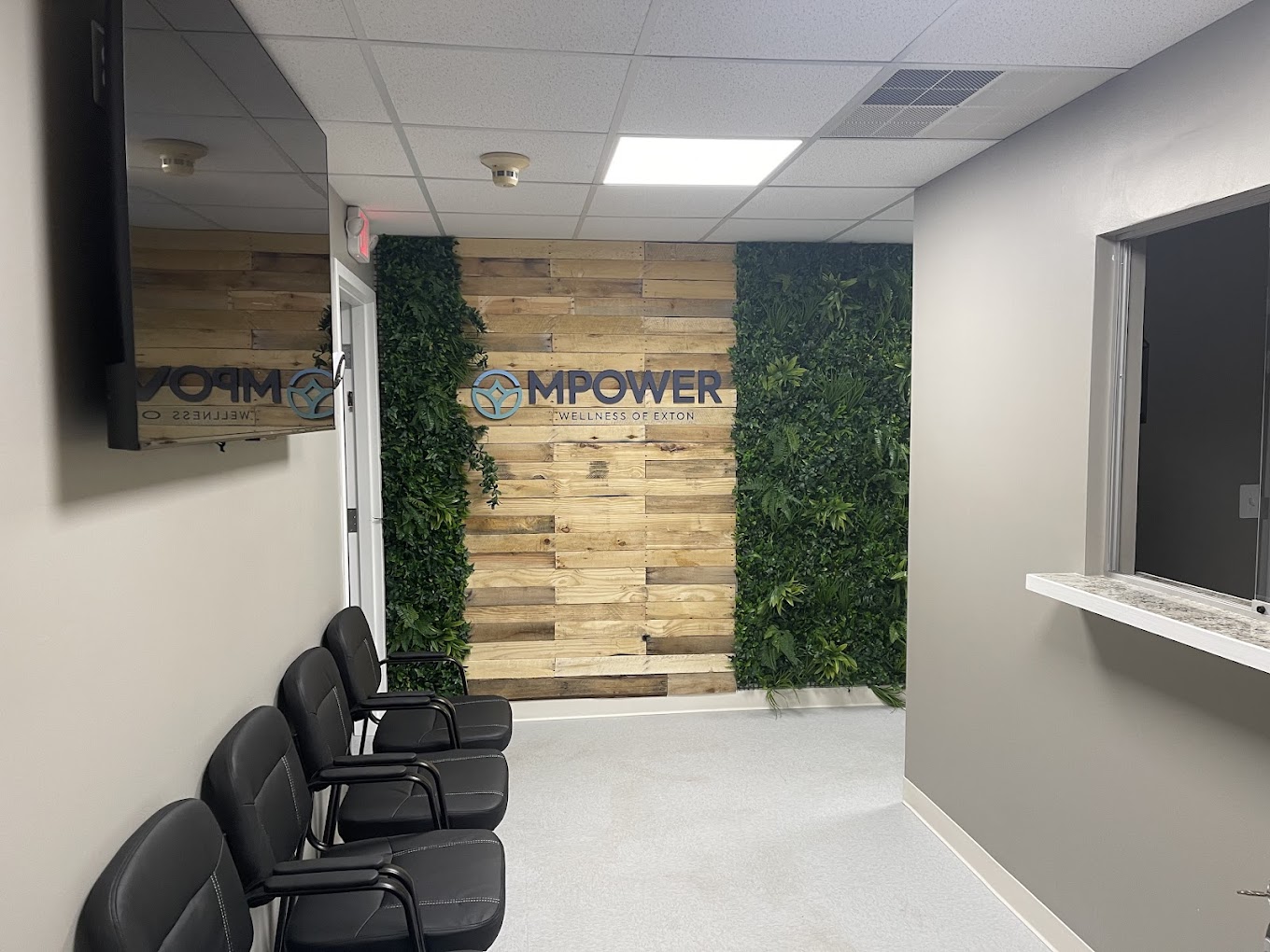 A waiting area with chairs, a reception window, and greenery decor.