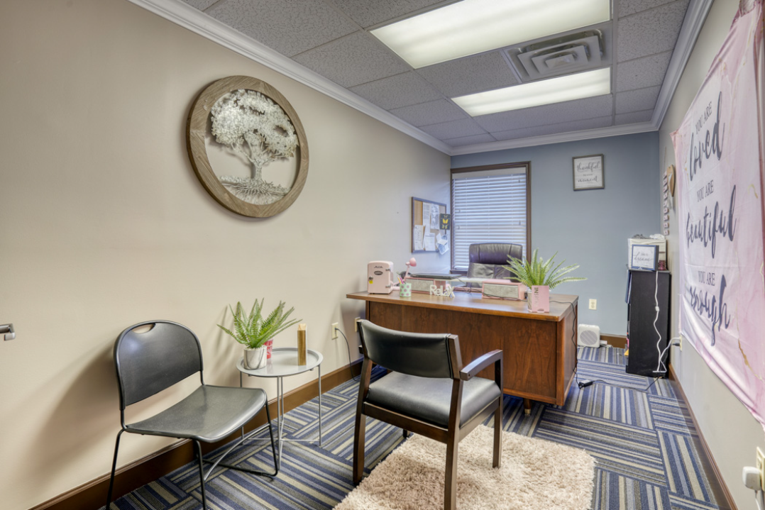 BrightView Health consultation room with desk, patient chairs, plants, wall decor, and blue patterned carpet