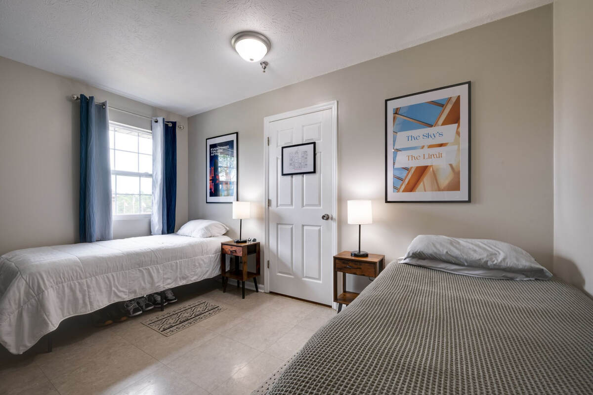 Twin bedroom with a window, blue curtains, and framed wall art.