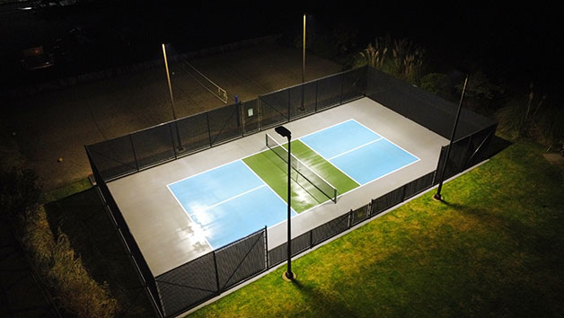 A lit-up pickleball court at night with surrounding greenery.