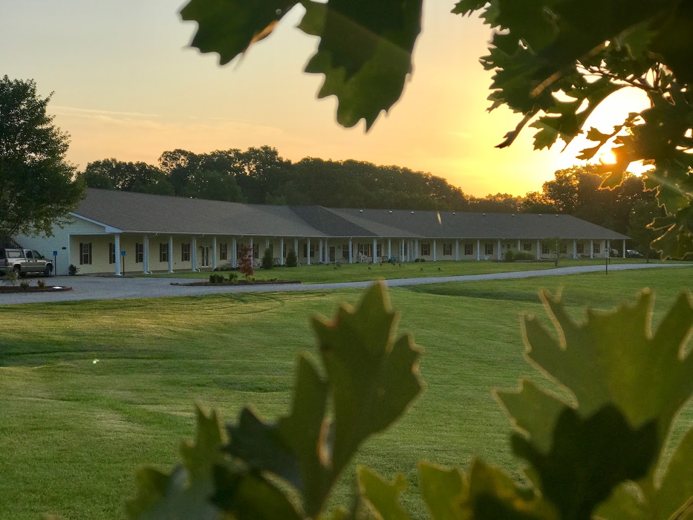 A rehab facility at sunset with a large lawn and wrap-around porch.