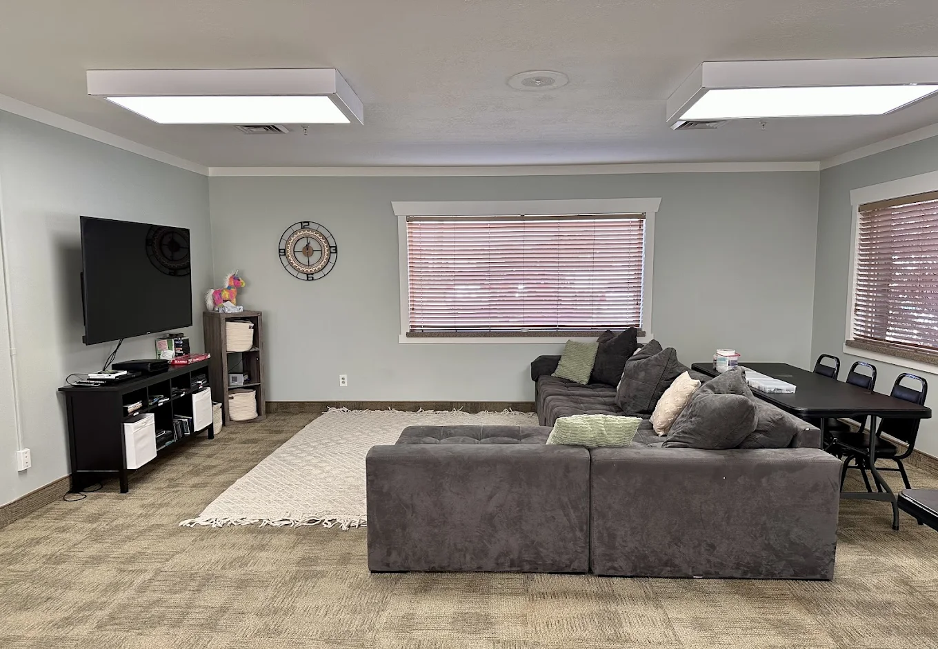 Common lounge with large sectional sofa, entertainment setup, and group table at New Roads Behavioral Health