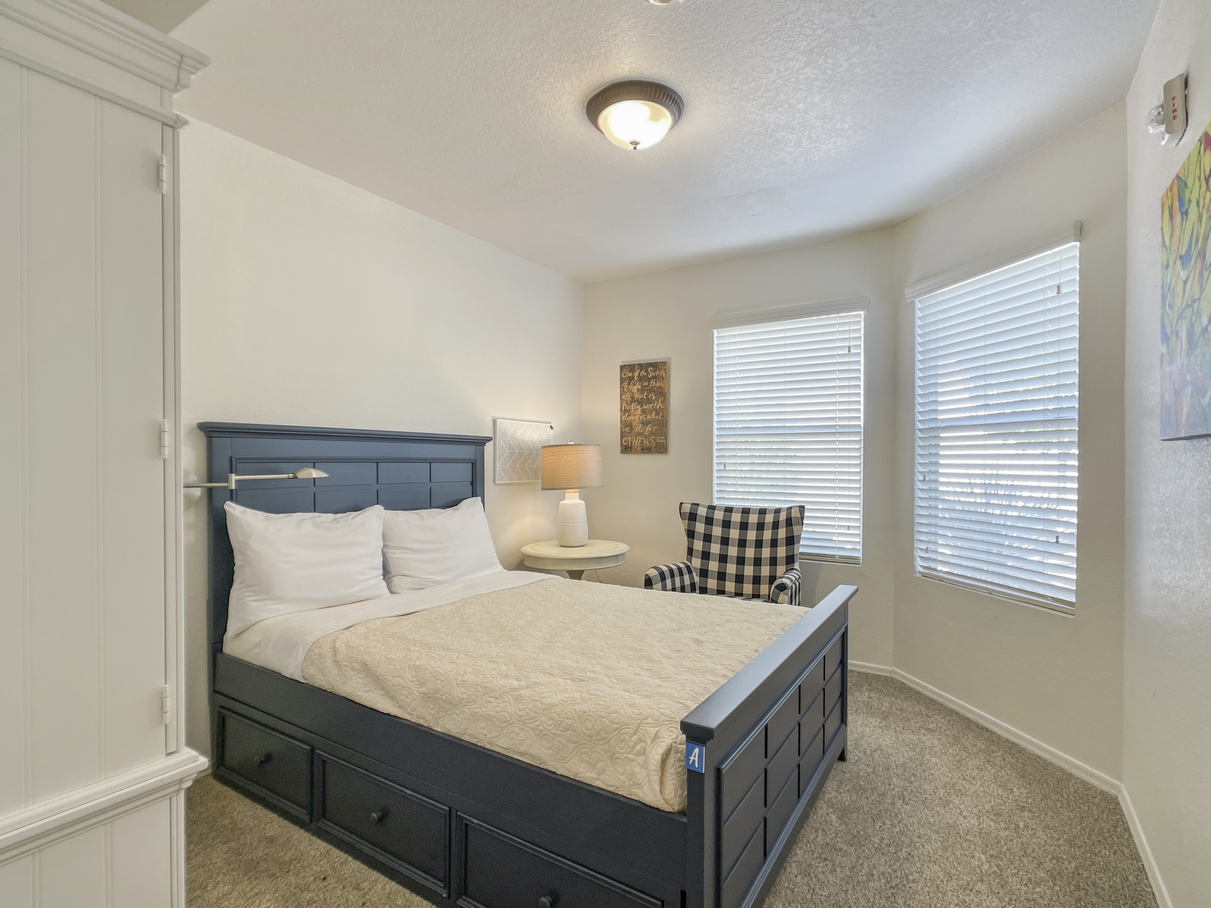 Bedroom witha made bed , an armchair, and a lamp.