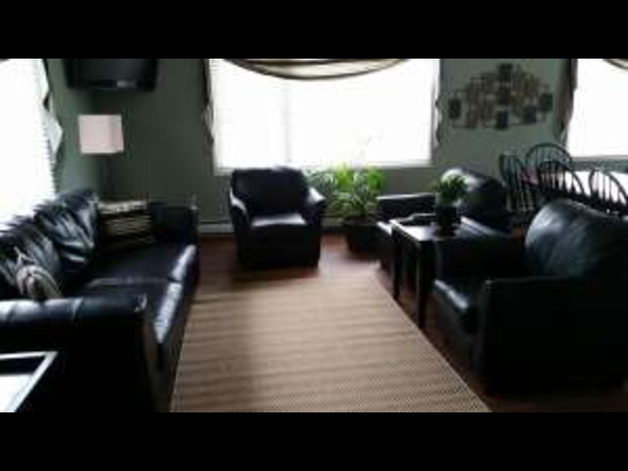 Living room with leather sofas and armchairs near large windows.