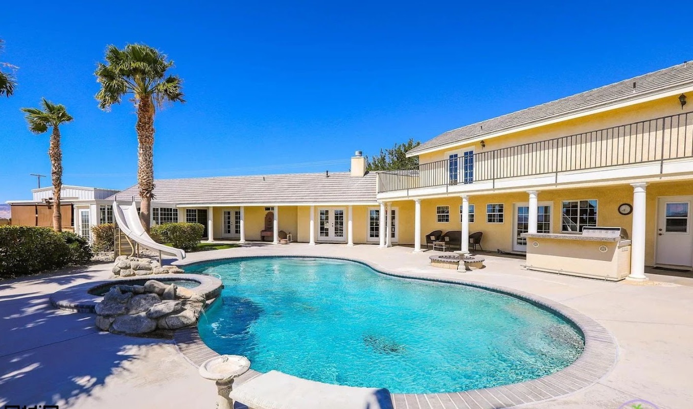Backyard pool with slide, hot tub, and palm trees