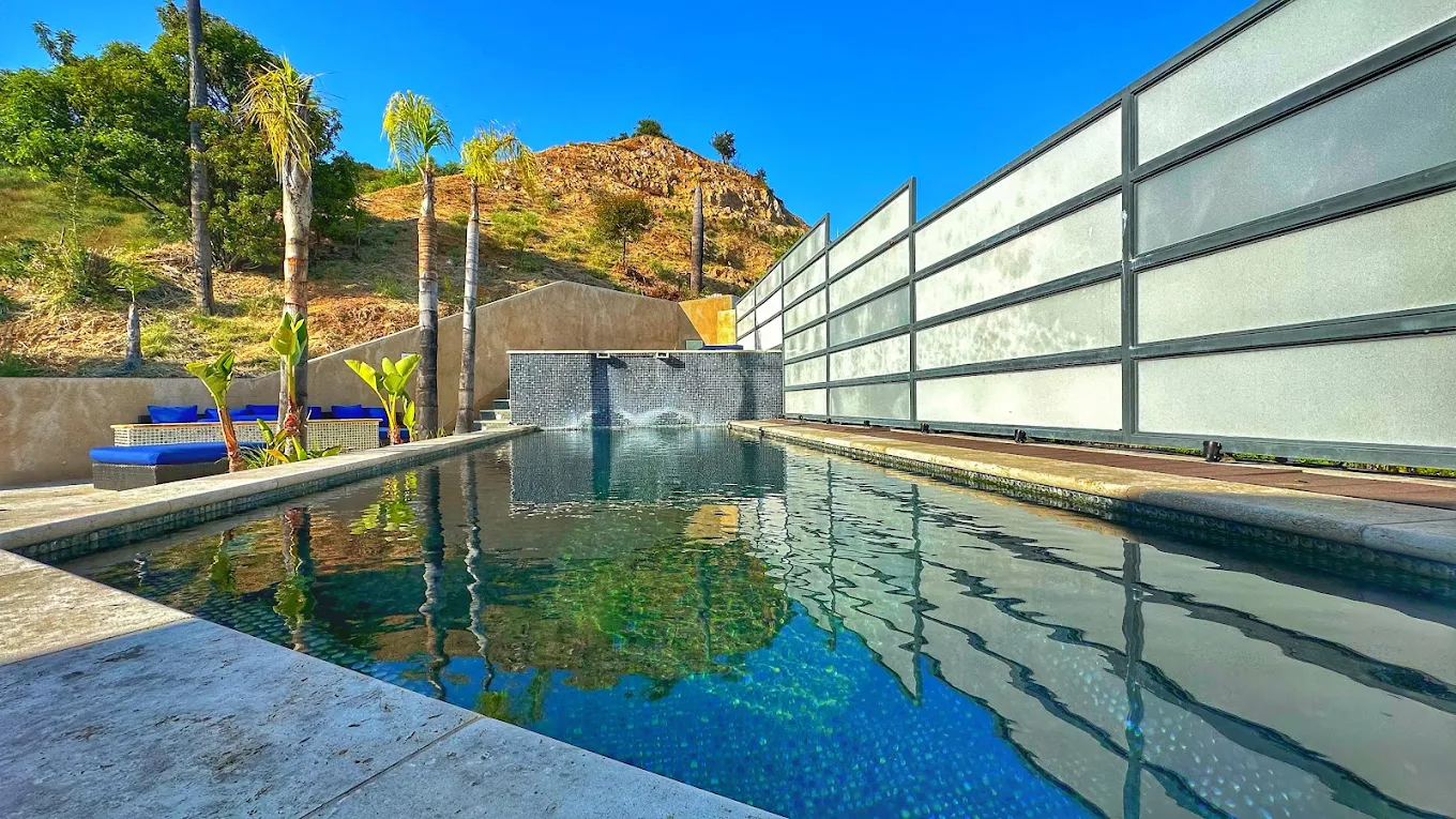 Outdoor swimming pool surrounded by palm trees and lounge seating with hillside views