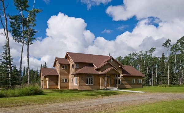 Two-story wooden residential treatment facility surrounded by trees under a bright sky