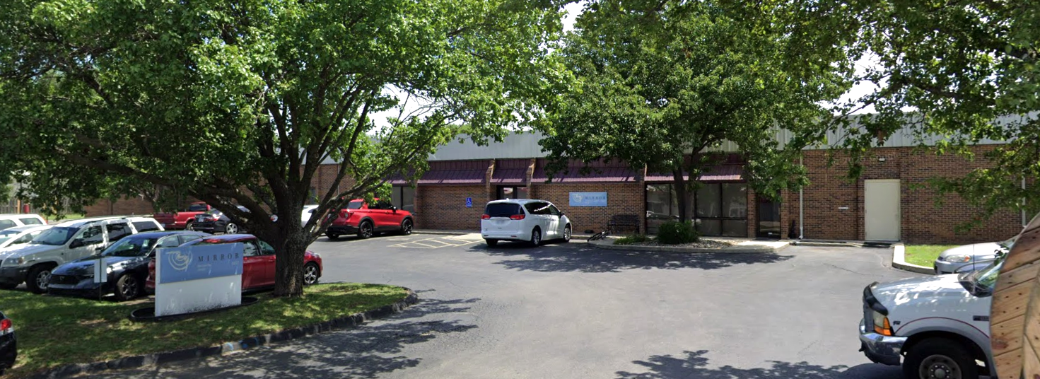 Brick rehab facility with trees and parked cars