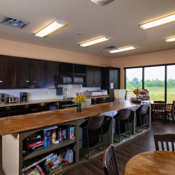 Kitchen area with bar seating, dining tables, and open shelves stocked with board games and snacks