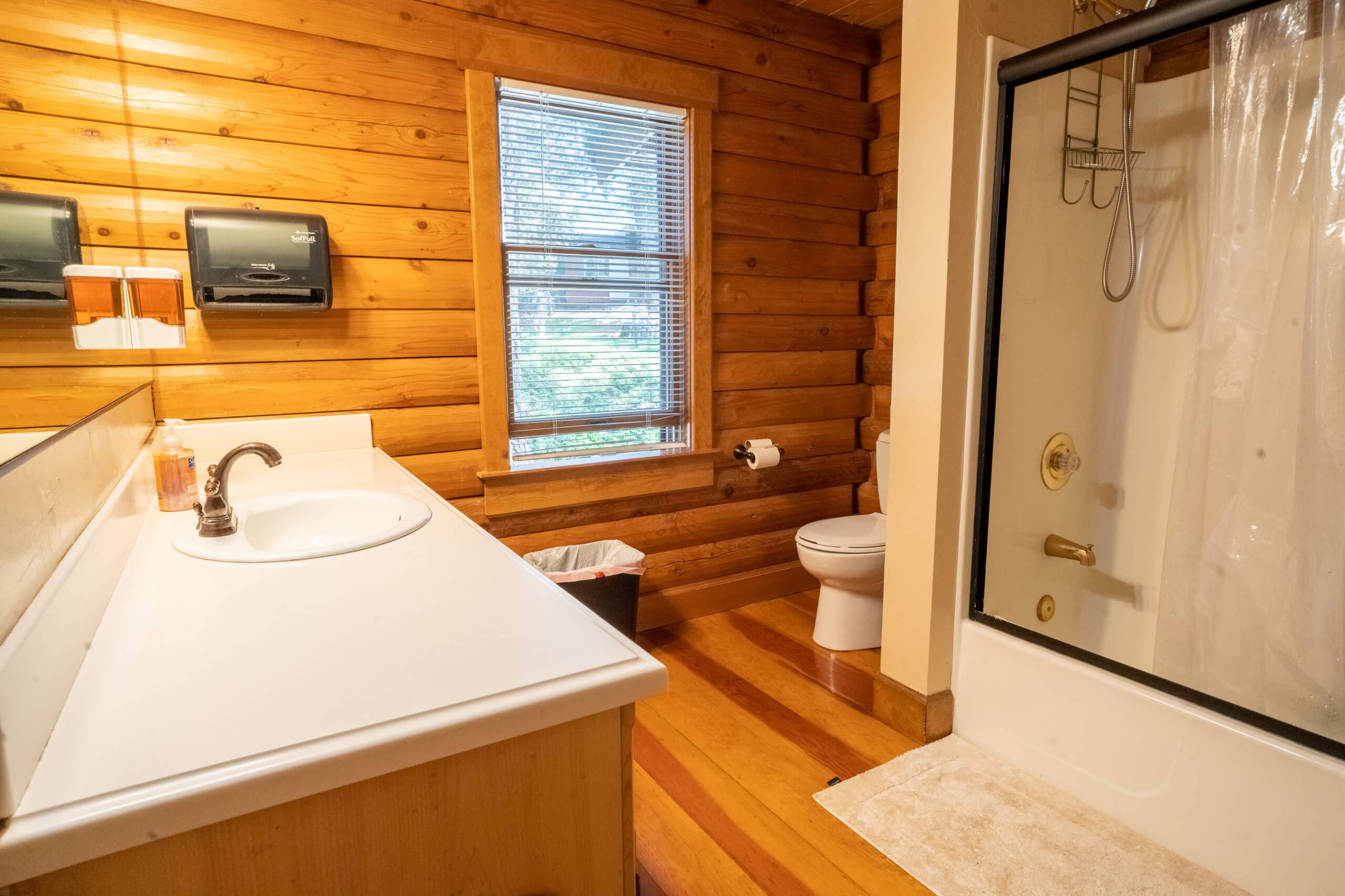 Private bathroom with wooden walls, white countertop sink, shower with glass doors, and natural light