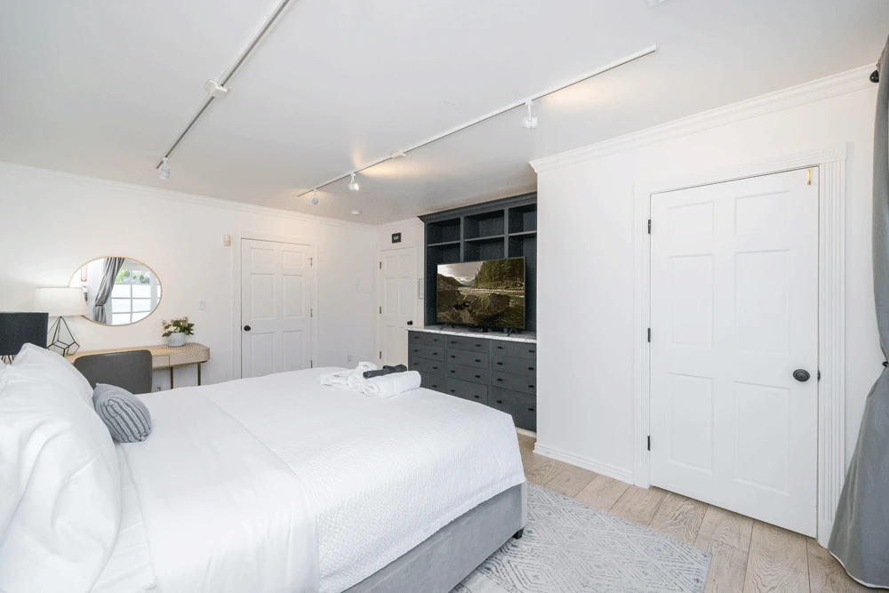 White bedroom with desk, TV, and built-in drawers
