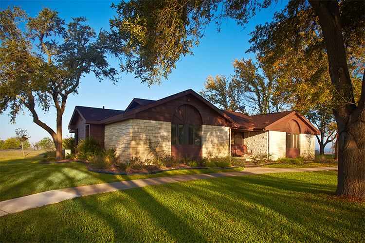 Front view of a stone cabin with trees and manicured lawn