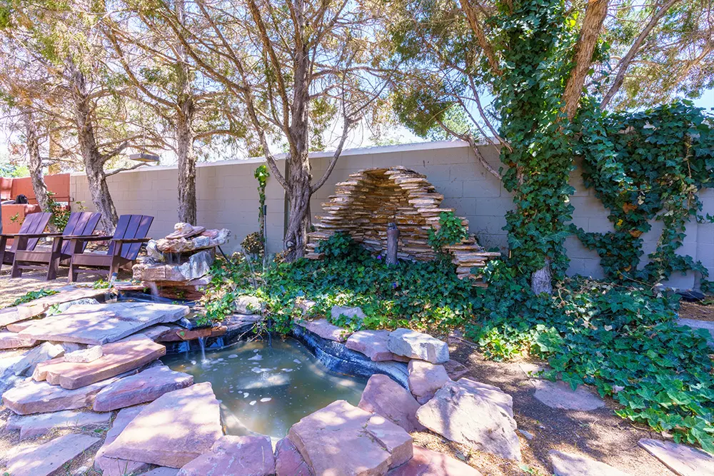 Small stone garden pond with waterfall and shaded seating
