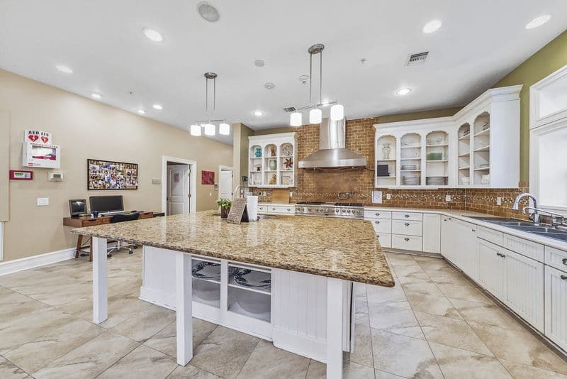 Bright kitchen with granite island, white cabinetry, and stainless steel appliances