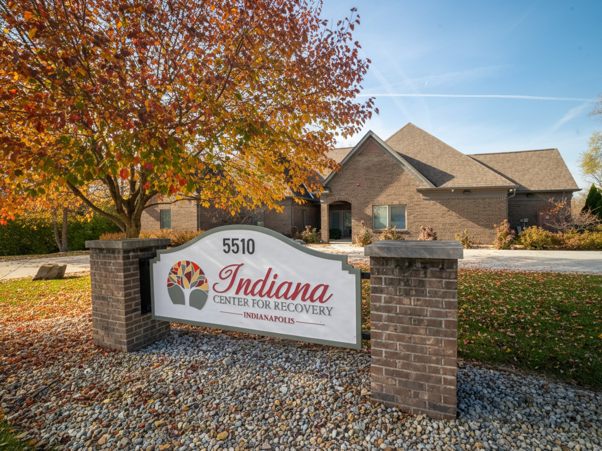 Facility sign in front of brick building with fall leaves.