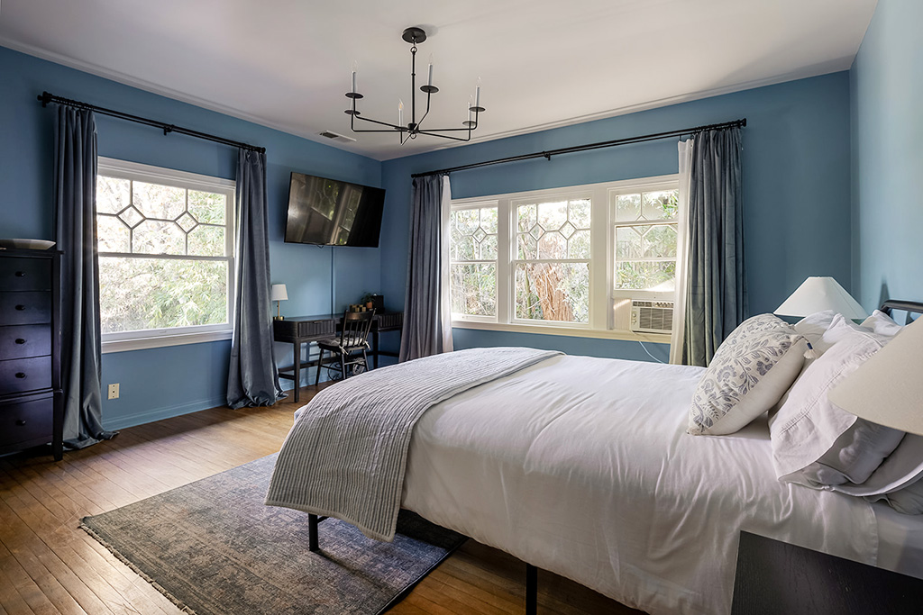 Bedroom with white bed, blue walls, large windows, and natural light