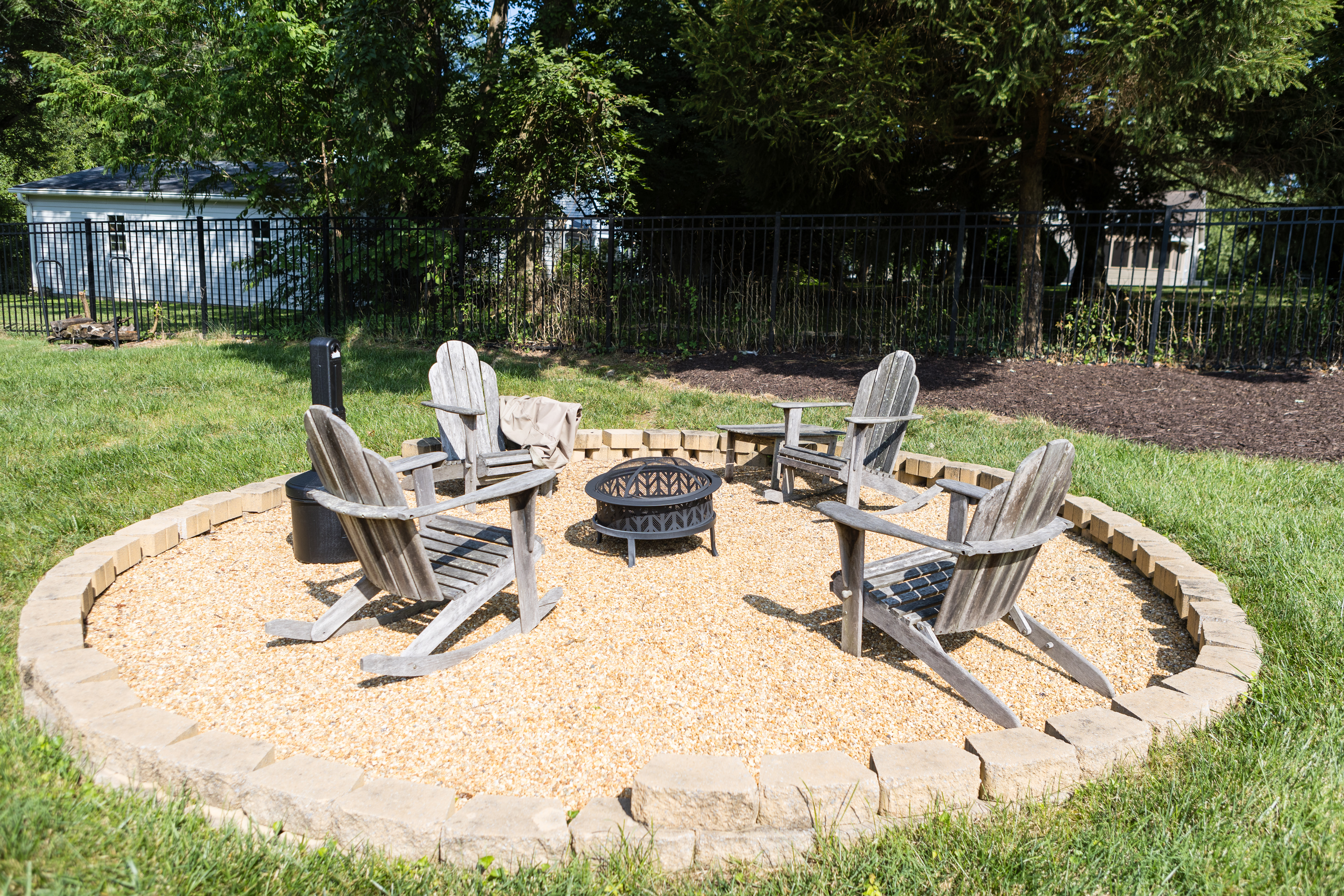 Firepit with wooden chairs on gravel in fenced backyard