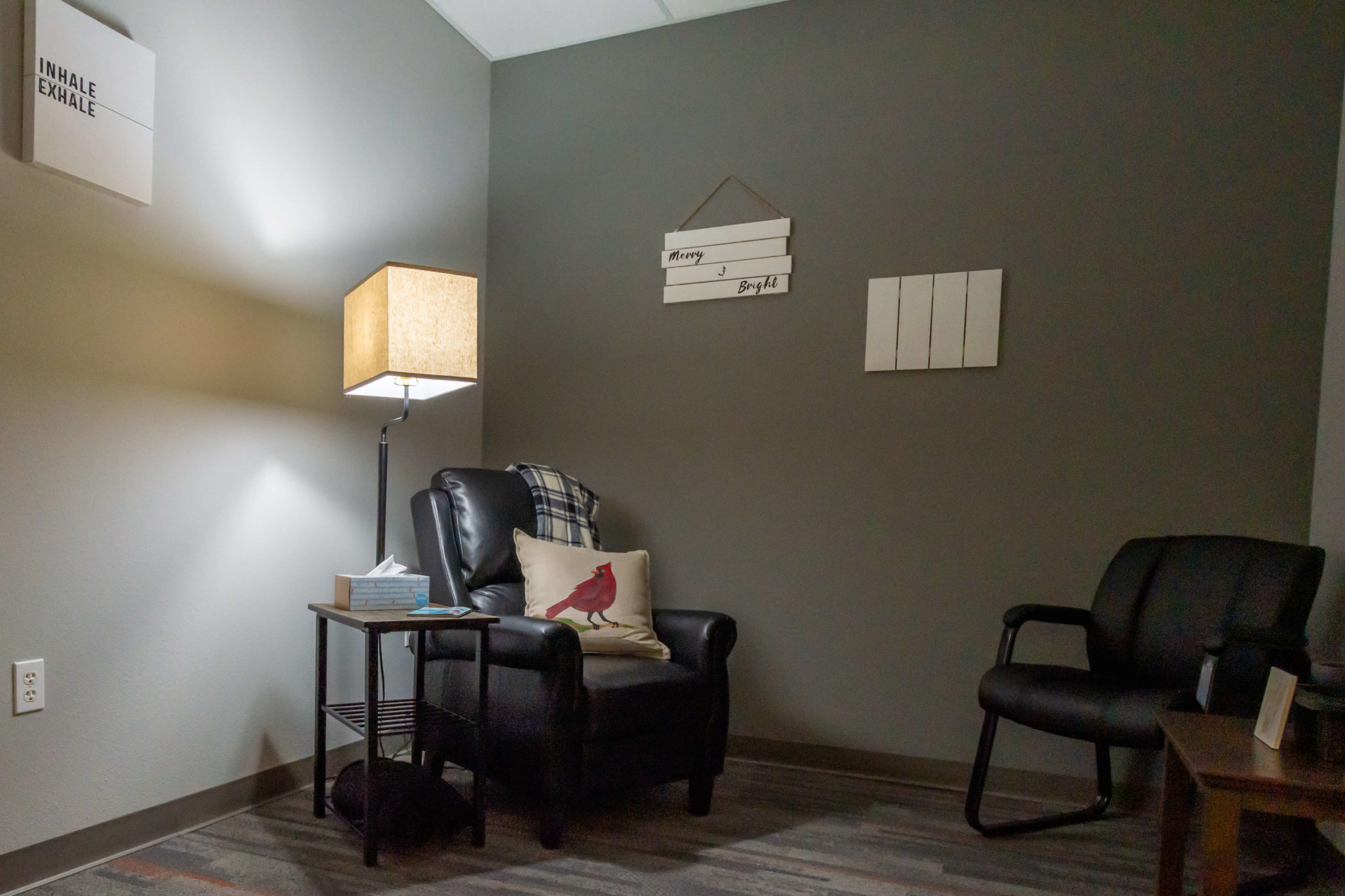 A cozy counseling room with a leather chair, lamp, and wall decor.