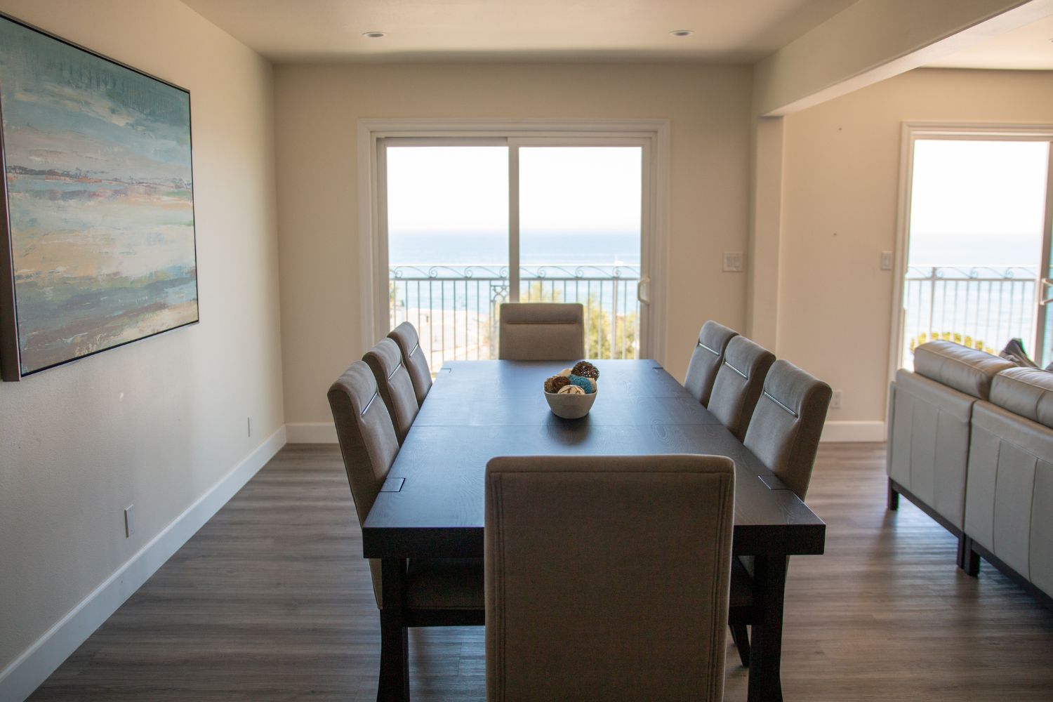 Elegant dining area with a table set for six, complemented by an ocean view through sliding doors, creating a serene, inviting space.