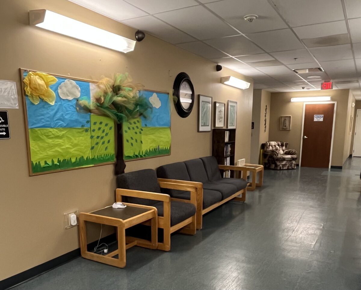 Rehab hallway with bulletin board and wood-framed chairs