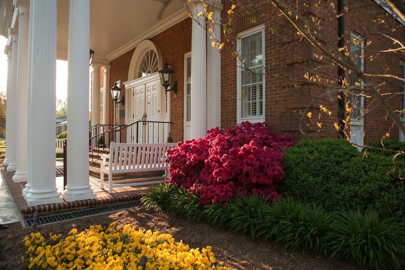 Entrance to facility showing seating at door, and flowers in a graden.