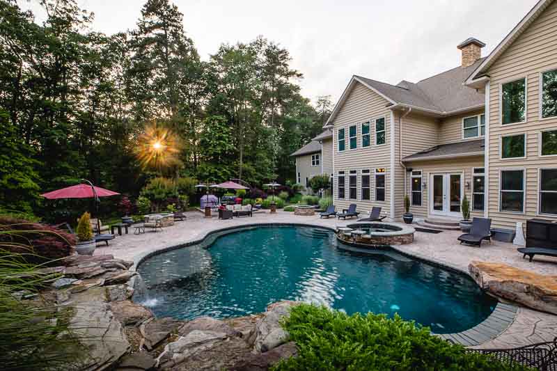 Backyard pool area with loungers, greenery, and stone accents