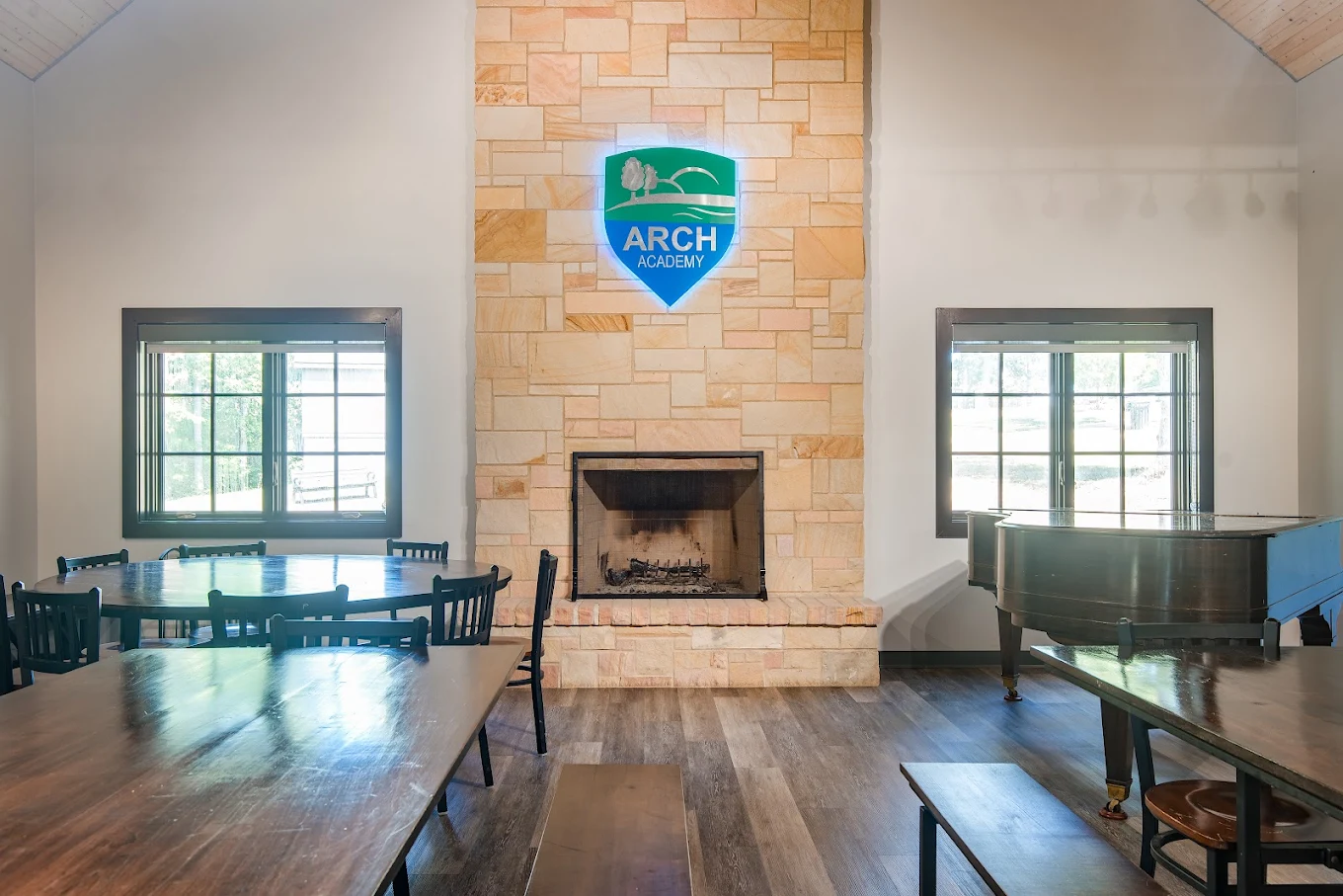 Dining hall with stone fireplace and grand piano at ARCH Academy.