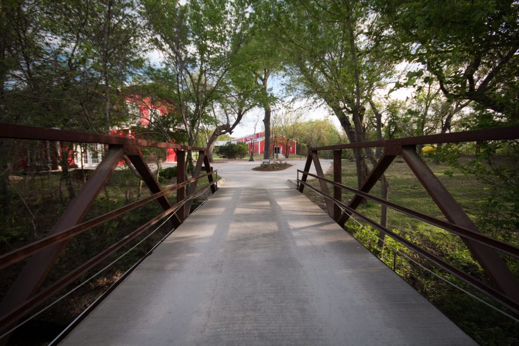 Tree-lined bridge path leading to red buildings