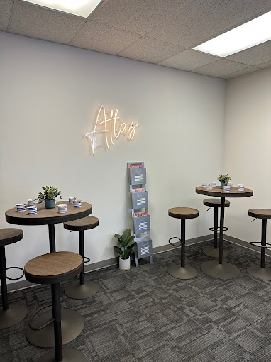 A social lounge with high-top tables, stools, and a neon "Atlas" sign.
