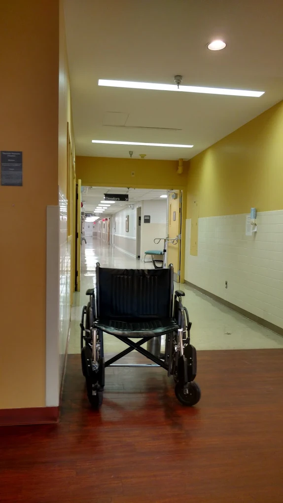 Yellow hospital hallway with wheelchair near elevator signs
