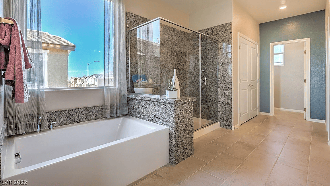 Modern bathroom with soaking tub, glass-enclosed shower, tiled flooring, and large window