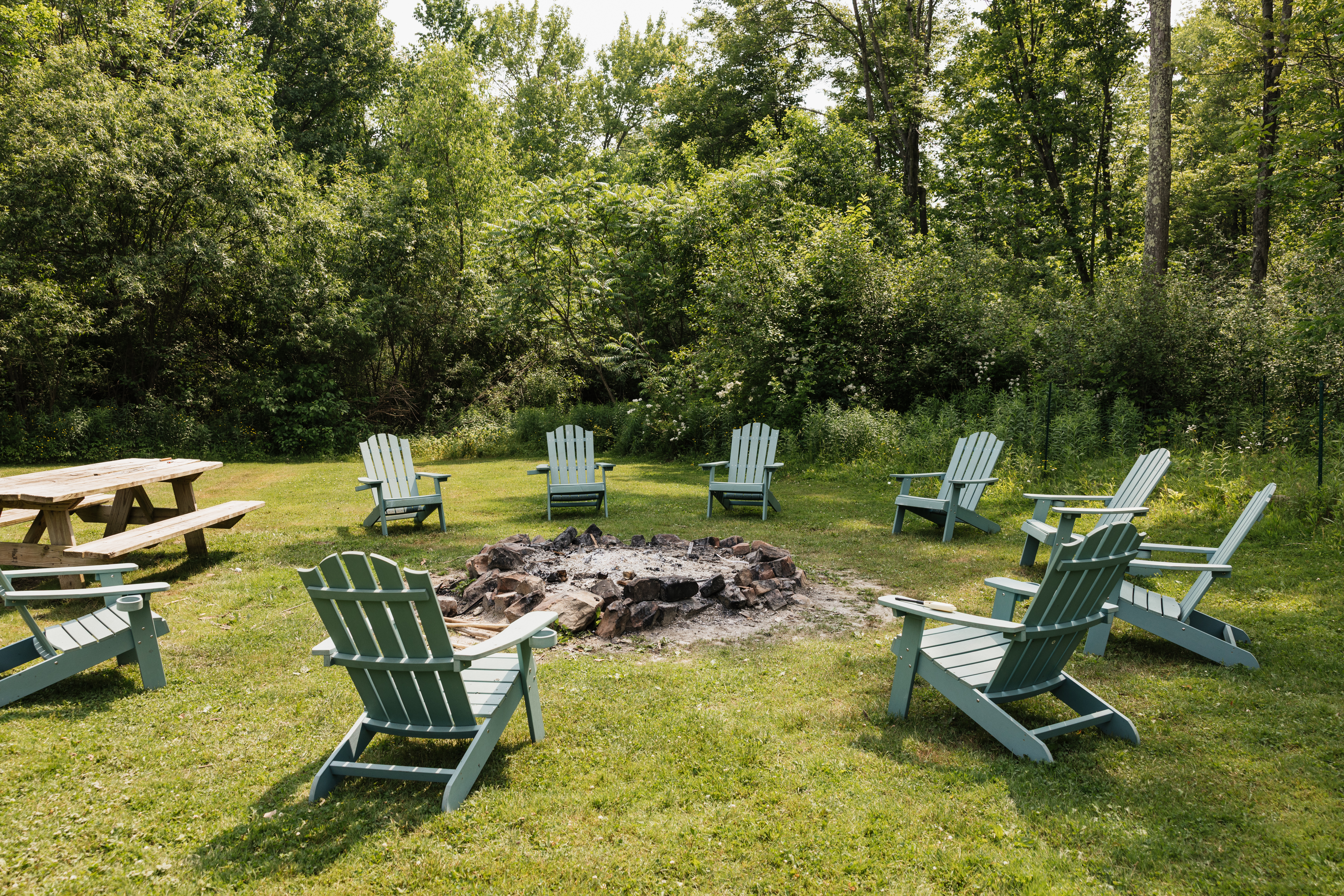 Adirondack chairs around fire pit in grassy area