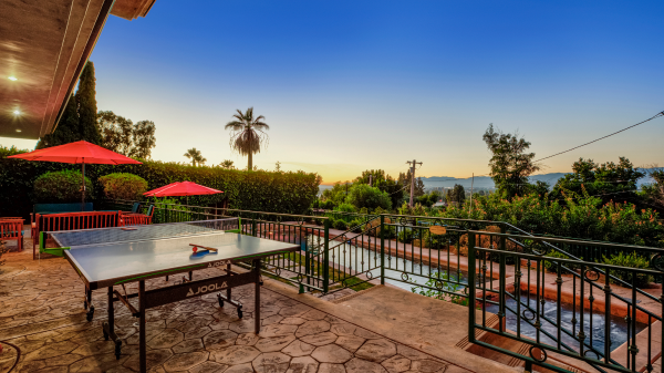 Patio with table tennis, red umbrellas, and scenic view of palm trees and mountains at sunset
